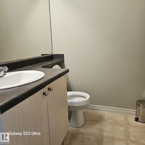 Bathroom vanity with an integrated white sink, dark countertop, and light wood-finish cabinetry - 99 13825 155 Avenue, Edmonton, AB 