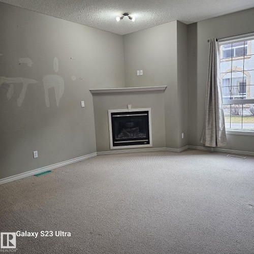 Living area featuring an integrated fireplace with a white mantel, light grey walls, and neutral carpeting - 99 13825 155 Avenue, Edmonton, AB 