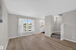 Spacious living area featuring wood-finish flooring, light grey walls, and ample natural light from the large windows - 