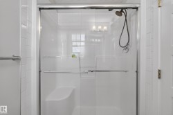 White shower enclosure featuring a built-in bench, clear glass doors, and a handheld shower fixture - 