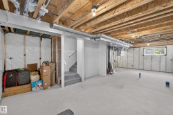 Unfinished basement with exposed ceiling joists and ductwork, concrete flooring, and a visible staircase - 
