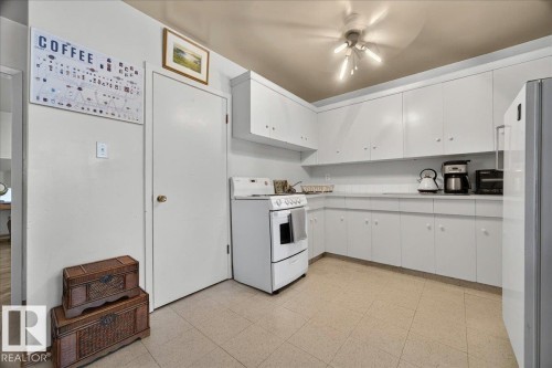 Bright kitchen featuring extensive white cabinetry, a white electric range, white countertops, a stainless steel refrigerator, and neutral tile flooring - 33 10230 122 Street, Edmonton, AB 