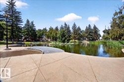 Lush green space featuring a reflective pond, mature evergreen trees, and a curved concrete pathway - 