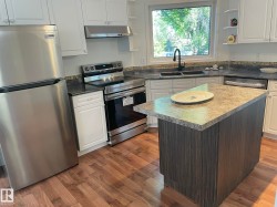 Kitchen featuring white cabinetry, stainless steel appliances, a central island with a contrasting base, wood-finish flooring, and a window above the sink - 