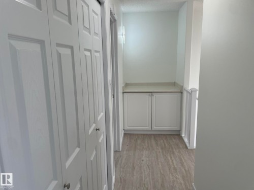 Hallway featuring white bi-fold doors, wood-finish flooring, and a built-in storage cabinet with a light-toned countertop - 2 1295 Carter Crest Road, Edmonton, AB - Indoor Photo Showing Other Room