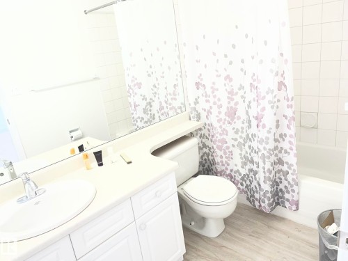 Bathroom featuring a vanity with an integrated sink, a rectangular mirror, a toilet, a full-size bathtub, and wood-finish flooring - 2 1295 Carter Crest Road, Edmonton, AB - Indoor Photo Showing Bathroom