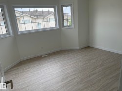 Spacious room featuring light wood-finish flooring, crisp white walls, and multiple windows with white trim - 