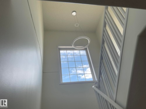 High ceilings featuring a prominent window with grid panes, a modern circular pendant light fixture, and a contemporary slatted staircase railing - 2 1295 Carter Crest Road, Edmonton, AB - Indoor