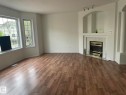 Spacious living area featuring wood-finish flooring, a bay window with multiple panes, a fireplace with a tiled surround, an integrated arched niche, and track lighting - 2 1295 Carter Crest Road, Edmonton, AB  - Indoor Photo Showing Living Room With Fireplace 