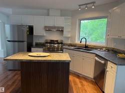 Modern kitchen featuring white cabinetry, a central island with wood-finish paneling, stainless steel appliances, and wood-finish flooring - 