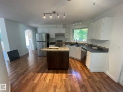 Open-concept kitchen featuring wood-finish flooring, white cabinetry, dark countertops, and a central island with a contrasting wood base and light-colored countertop - 