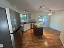Open-concept kitchen featuring wood-finish flooring, white cabinetry, granite-finish countertops, stainless steel appliances, and a central island with breakfast bar seating - 
