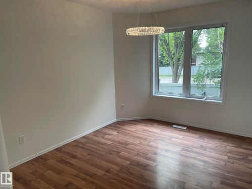 Bright room featuring a large window, a contemporary chandelier, wood-finish flooring, and white baseboards - 2 1295 Carter Crest Road, Edmonton, AB - Indoor Photo Showing Other Room