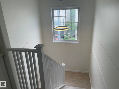Staircase featuring wood-finish flooring, white banister with squared newel post, a large window with grid pattern, and a contemporary circular pendant light fixture - 2 1295 Carter Crest Road, Edmonton, AB - Indoor Photo Showing Other Room
