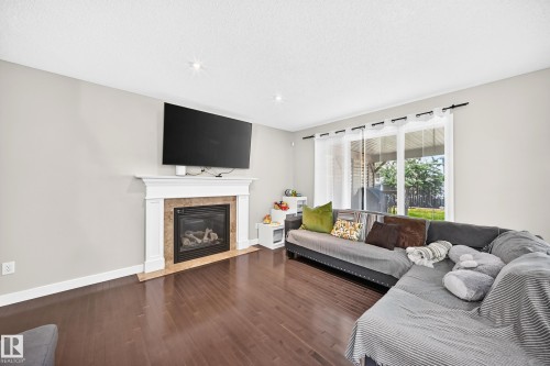Living space featuring wood-finish flooring, a fireplace with a white mantel and stone surround, and recessed lighting - 3433 Goodridge Link Link, Edmonton, AB 