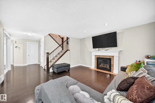 Living space featuring wood-finish flooring, a fireplace with a white mantel and stone surround, and recessed lighting - 3433 Goodridge Link Link, Edmonton, AB 