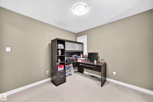 Neutral-toned room featuring a textured white ceiling, light carpeting, and a built-in office desk with accompanying shelving - 3433 Goodridge Link Link, Edmonton, AB 