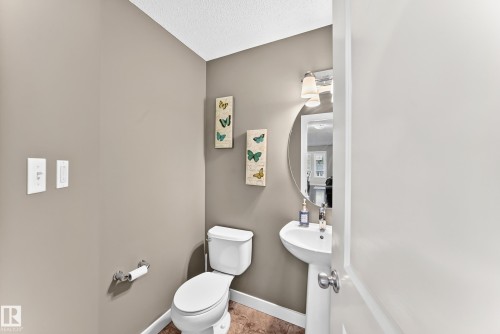Compact powder room featuring a white pedestal sink, circular wall mirror, and two-light vanity fixture - 3433 Goodridge Link Link, Edmonton, AB 