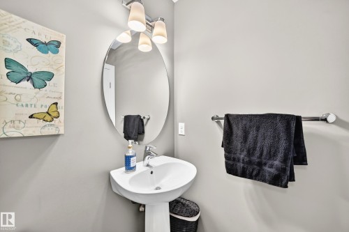 Pedestal sink with a polished chrome faucet, oval mirror, and contemporary vanity lighting - 3433 Goodridge Link Link, Edmonton, AB 