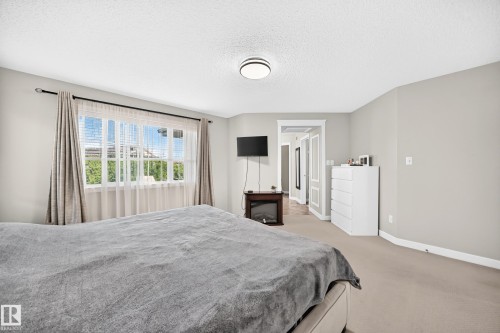 Spacious bedroom with a large window, neutral wall tones, white trim, and a ceiling-mounted light fixture - 3433 Goodridge Link Link, Edmonton, AB 