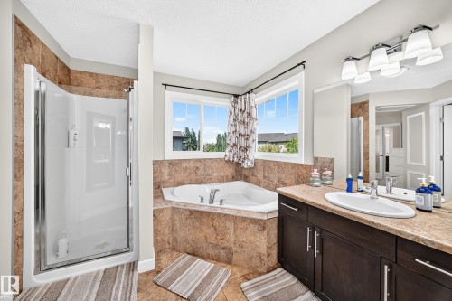 Bathroom featuring a corner soaking tub, a separate shower with a glass enclosure, a single vanity with a countertop, and a vanity mirror with overhead lighting - 3433 Goodridge Link Link, Edmonton, AB 