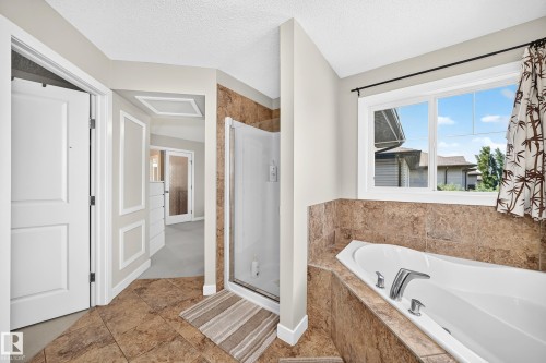 Bathroom featuring a built-in soaking tub with chrome fixtures, a glass-enclosed shower, and large format floor tiling - 3433 Goodridge Link Link, Edmonton, AB 