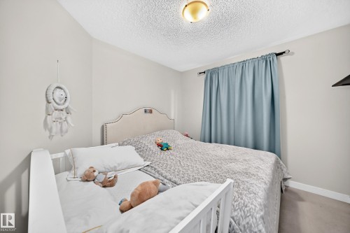 Bedroom featuring a light gray upholstered headboard, ceiling-mounted light fixture, and light blue window treatments on a dark rod - 3433 Goodridge Link Link, Edmonton, AB 
