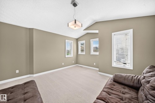 Spacious room featuring vaulted ceilings, a contemporary ceiling light fixture, multiple windows with white blinds, neutral wall tones, and light-colored carpeting - 3433 Goodridge Link Link, Edmonton, AB 