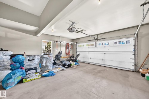 Spacious garage featuring a concrete floor, light gray walls, and an overhead garage door with upper window inserts - 3433 Goodridge Link Link, Edmonton, AB 