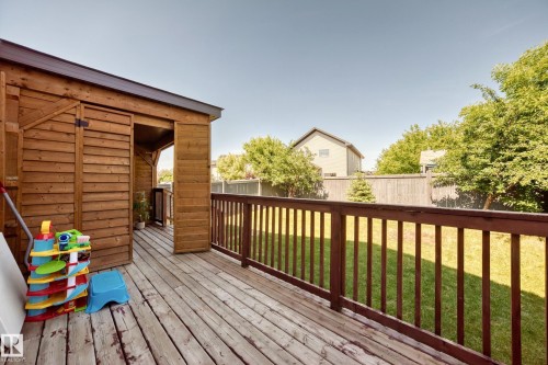 Expansive wood deck with a built-in storage shed, featuring a dark wood railing and a spacious green lawn - 3433 Goodridge Link Link, Edmonton, AB 