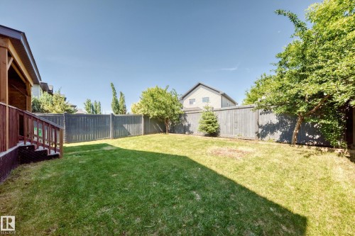 Spacious fenced backyard featuring a manicured lawn, established trees, and a covered wood deck with stairs - 3433 Goodridge Link Link, Edmonton, AB 