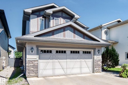Modern multi-level residence featuring a double garage with frosted glass panels, stone veneer accents, horizontal siding, and a gabled roofline - 3433 Goodridge Link Link, Edmonton, AB 