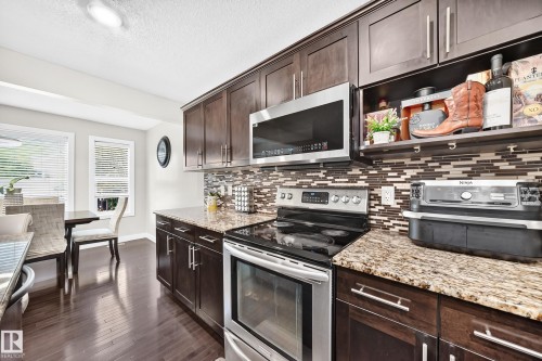 Modern kitchen featuring dark wood cabinetry, granite countertops, and a mosaic tile backsplash - 3433 Goodridge Link Link, Edmonton, AB 