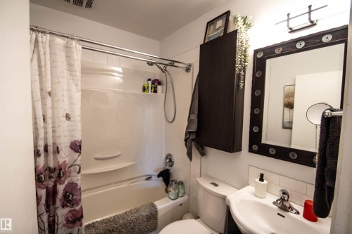 Bathroom featuring a white bathtub with an integrated shower, a wall-mounted sink, a toilet, and a dark-framed mirror - 5217 47 Ave, St. Paul Town, AB 