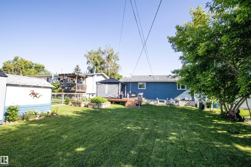 Expansive grassy backyard featuring a wooden deck with gazebo, raised garden beds, and a storage shed - 5217 47 Ave, St. Paul Town, AB 
