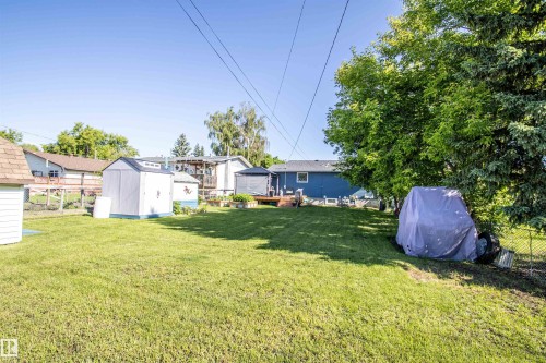 Expansive backyard featuring a manicured lawn, two storage sheds, and mature trees providing ample shade - 5217 47 Ave, St. Paul Town, AB 