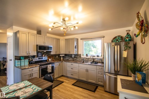 Kitchen featuring light gray cabinetry, stainless steel appliances, granite-style countertops, and a full tile backsplash - 5217 47 Ave, St. Paul Town, AB 