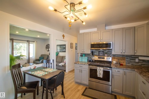 Open-concept kitchen featuring gray shaker-style cabinetry, stainless steel appliances, a multi-tone tile backsplash, and wood-finish flooring - 5217 47 Ave, St. Paul Town, AB 