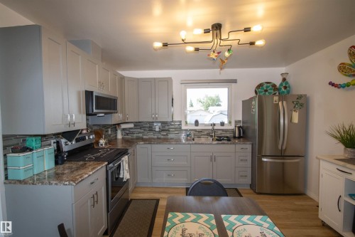 Contemporary kitchen featuring light gray cabinetry, stainless steel appliances, a mosaic tile backsplash, and wood-finish flooring - 5217 47 Ave, St. Paul Town, AB 