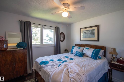 Bedroom featuring a white ceiling fan with integrated lighting, a double window with gray curtains, and a wood-finish headboard - 5217 47 Ave, St. Paul Town, AB 