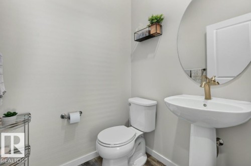 Pedestal sink with a gold-tone faucet, round wall mirror, and wood-finish flooring - 2116 Maple Road, Edmonton, AB 