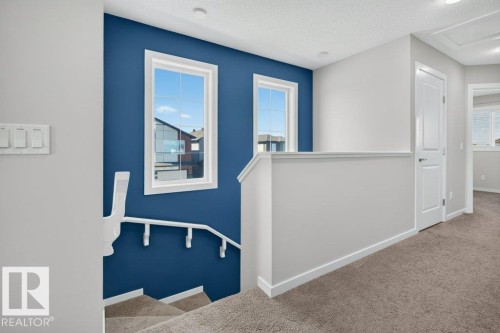 Upper-level landing featuring a carpeted floor, white trim, and a vibrant accent wall with two windows - 2116 Maple Road, Edmonton, AB 