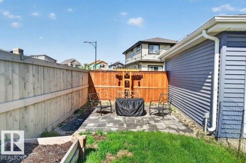 Paved patio area featuring a wooden privacy fence, a raised garden bed, and a grass lawn - 2116 Maple Road, Edmonton, AB 