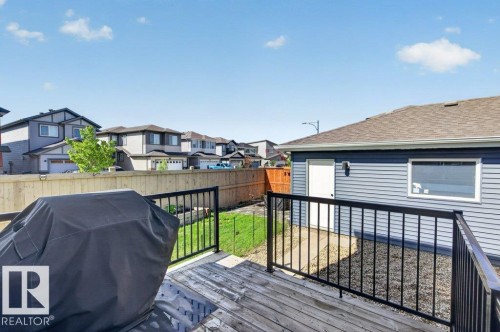 Wood-finish deck with black metal railing, featuring a detached garage with blue siding and a brown shingle roof, and a fenced yard with a patch of green lawn - 2116 Maple Road, Edmonton, AB 