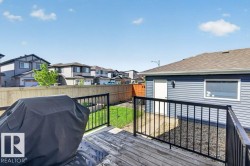 Wood-finish deck with black metal railing, featuring a detached garage with blue siding and a brown shingle roof, and a fenced yard with a patch of green lawn - 