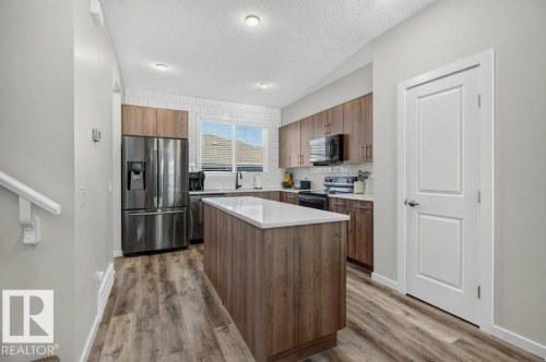 Contemporary kitchen featuring a center island with a white countertop, wood-finish flooring, stainless steel appliances, a subway tile backsplash, and recessed lighting - 2116 Maple Road, Edmonton, AB 