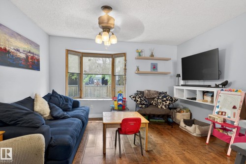 Living area featuring wood-finish flooring, a multi-pane bay window with privacy blinds, and a ceiling fan with integrated lighting - 9821 153 Street, Edmonton, AB - Indoor Photo Showing Living Room
