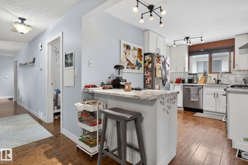 Kitchen with wood-finish flooring, white cabinetry, a built-in breakfast bar with a light-colored countertop, and a stainless steel dishwasher - 9821 153 Street, Edmonton, AB - Indoor Photo Showing Kitchen With Upgraded Kitchen