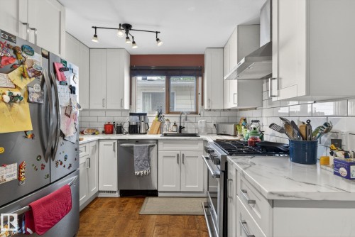 Modern kitchen featuring white shaker cabinetry, stainless steel appliances, marble-look countertops, subway tile backsplash, and wood-finish flooring - 9821 153 Street, Edmonton, AB - Indoor Photo Showing Kitchen