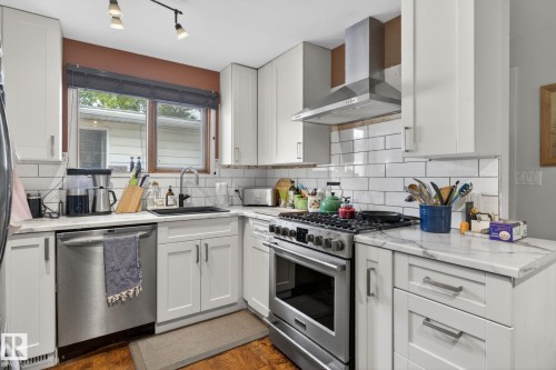 Kitchen featuring white shaker cabinetry, stainless steel appliances, marble-look countertops, subway tile backsplash, and wood-finish flooring - 9821 153 Street, Edmonton, AB - Indoor Photo Showing Kitchen With Upgraded Kitchen